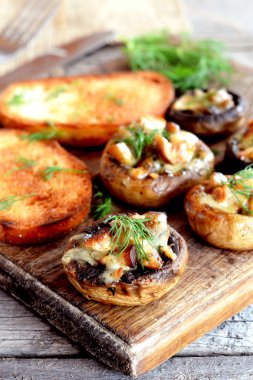 Sağlıklı peynir ve et mantar dolması ve kızarmış ekmek dilimleri bir ahşap kesme tahtası üzerinde. Ev yapımı mantar tarifi 