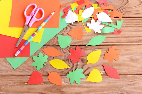 Färgade pappersark, sax, penna, lämnar höstens färgat papper på trä bakgrund. Klippa med sax. Utveckling av färdighet för ett småbarn eller förskolebarn. Ovanifrån — Stockfoto