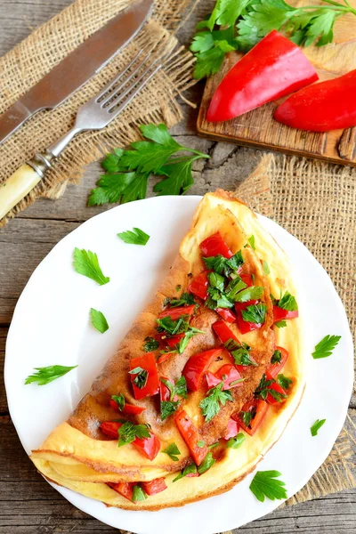 Tortilla de huevo rellena con verduras en un plato. Tortilla saludable con pimiento rojo frito, perejil fresco y especias. Tenedor, cuchillo sobre una arpillera y fondo de madera vieja. Receta de huevos fáciles. Vista superior — Foto de Stock