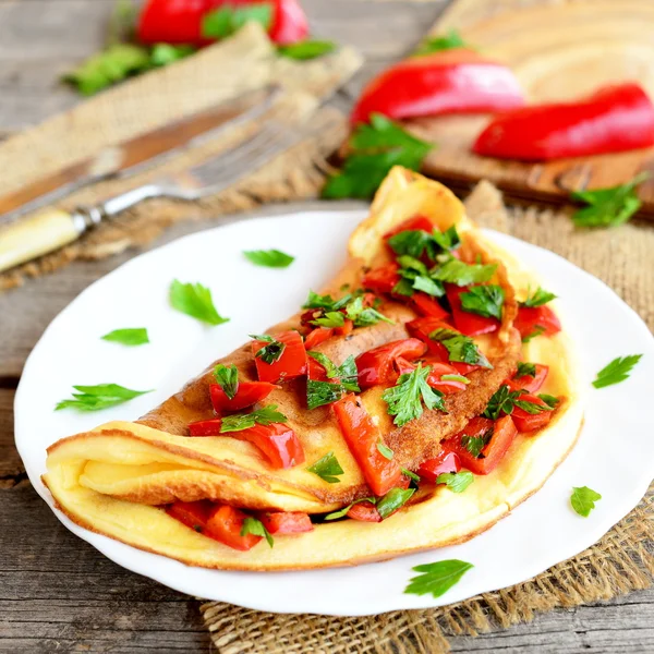 Omelet goreng dengan sayuran di piring, garpu dan pisau dengan latar belakang kayu tua. Omelet berwarna diisi dengan lada merah panggang dan peterseli segar cincang. Sarapan resep dengan telur. Penutup — Stok Foto