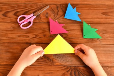 Origami renkli balık, makas. Çocuk elinde kağıt kağıt tutar ve origami balık yapma. Adım. Kahverengi ahşap arka plan 