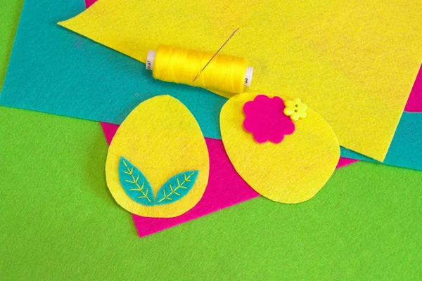 Пасхальный набор яиц, желтая нить, игла, цветочная пуговица, разноцветные войлочные простыни на зеленом фоне. Как сшить украшение пасхальных яиц. Интерьер дома. Швейные ремесла. Шаг — стоковое фото