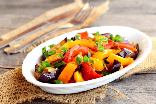 Vegetarischer Eintopf auf einem Teller und auf einem Holztisch. gedämpfte Auberginen, rote und orangefarbene Paprika und grüne Zwiebeln. Diätgericht. Gemüseeintopf. Nahaufnahme — Stockfoto