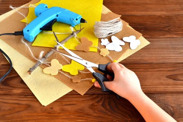 Kind hält die Schere in der Hand und schneidet die Filzblume aus. Schere, Heißklebepistole, Filzblätter, dekorativer Anhänger mit Filzschmetterlingen und Blumen — Stockfoto