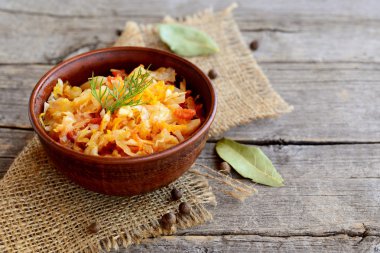 Kızarmış lahana bir kil kase ve eski ahşap zemin üzerinde. Lahana, havuç, domates ve sarımsak ile kızarmış ve ince dal dereotu ile süslenmiş. Bitkisel diyet yemek