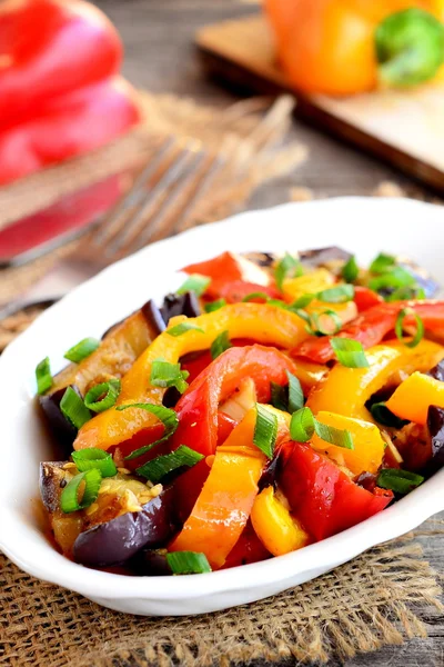 Vegetable stew on a plate. Diet stew with braised eggplant, red and orange peppers, garlic and green onion. Stewed vegetable mix. Hearty food. Wooden background. Closeup