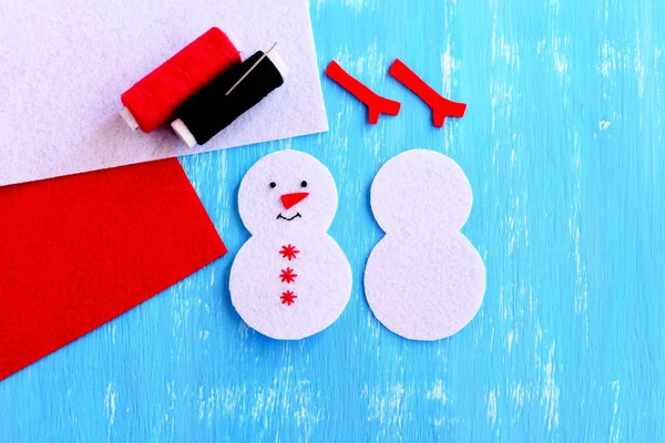 Cómo hacer un adorno de muñeco de nieve de Navidad. ¡Paso! Corte de fieltro blanco para adornos de Navidad hechos a mano. Por un lado bordado con hilo negro ojos y boca, hilo rojo copos de nieve y nariz — Foto de Stock