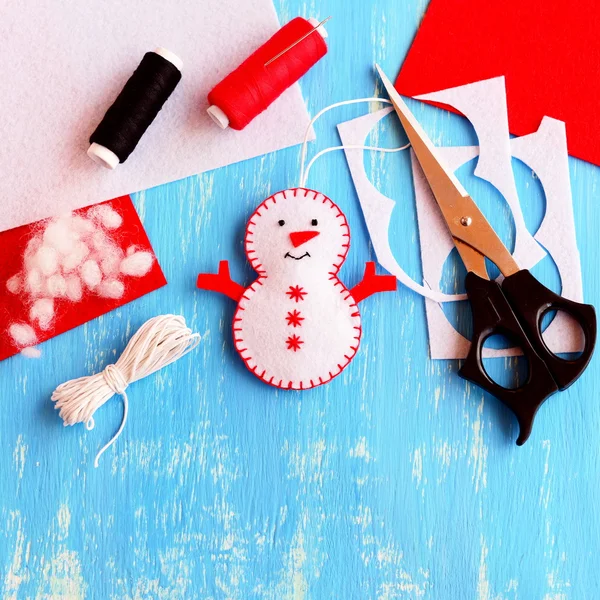 Sevimli bir Noel kardan adam süsü, makas, iplik, iğne, kordon, ahşap zeminde keçeli çarşaf ve kırıntılar. El yapımı kardan adam yapmak için malzeme dikiyorum. Noel çocukları el işi yapar. Noel çocukları geçmişi. Üst görünüm