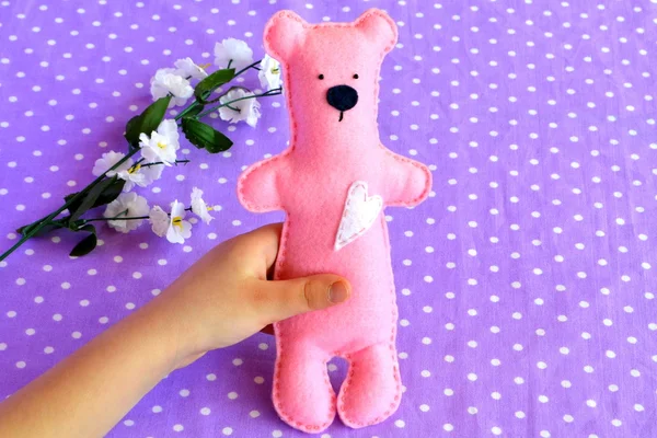 La niña sostiene al oso en su mano. Niño pequeño sostiene un osito de peluche de fieltro rosa en la mano —  Fotos de Stock