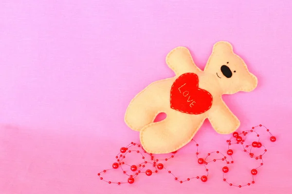 Boneka beruang buatan tangan. Beige merasa beruang di latar belakang merah muda, tangan dijahit mainan, kerajinan dari merasa — Stok Foto