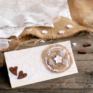 Rustik düğün davetiye kartı eski ahşap zemin üzerinde. Orijinal düğün davetiye kartı yapılan karton, dantel, çuval bezi, ahşap Kalpler, plastik çiçek. Portre