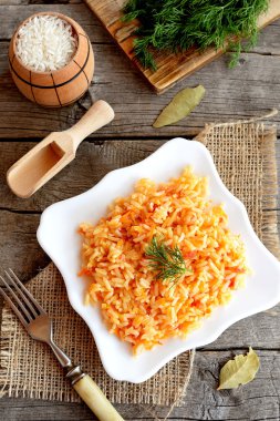 Bir tabak, çatal, yeşil dereotu, eski ahşap arka plan üzerinde kesme tahtası üzerinde sebze risotto. Domates, havuç, sarımsak ve baharat ile pişmiş pirinç. Kolay vejetaryen risotto tarifi 