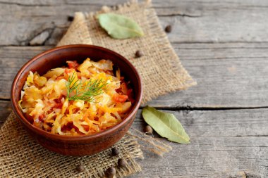 Kızarmış lahana bir kapta ve eski ahşap zemin üzerinde. Lahana, havuç, domates ve sarımsak ile kızarmış ve ince dal dereotu ile süslenmiş. Sebze tabağı 