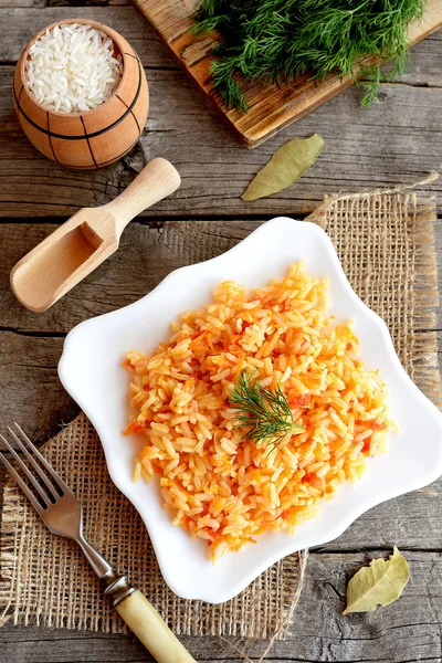 Gemüserisotto auf einem Teller, Gabel, grünem Dill, Schneidebrett auf altem Holzgrund. Reis mit Tomaten, Karotten, Knoblauch und Gewürzen gekocht. einfaches vegetarisches Risotto-Rezept — Stockfoto
