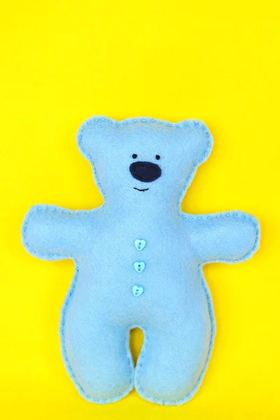 Blue felt bear on yellow background, hand-stitched toys, a craft out of felt. Boneka buatan tangan beruang teddy. DIY boneka beruang kerajinan proyek menjahit mudah — Stok Foto