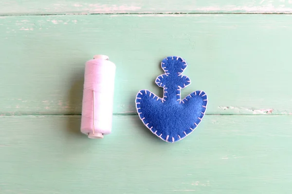 Ancla de fieltro azul, hilo blanco, aguja sobre fondo de madera. Dos piezas de fieltro en forma de ancla cosida con hilo blanco. Artesanía básica de costura para niños. Tutorial. Paso. — Foto de Stock