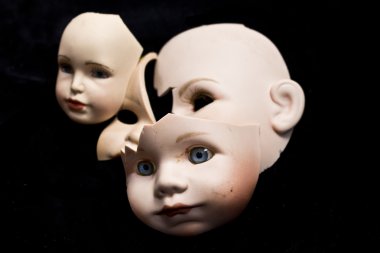 Close Up of Broken Doll Heads and Parts On Black Background clipart