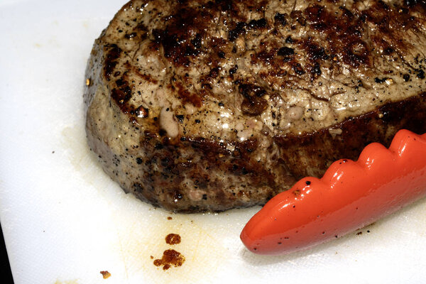 Close up of seasoned cooked steak resting on a white chopping board