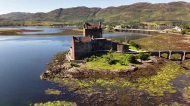 Hava görüntüsü, Eilean Donan Kalesi 'nin küçük bir adada tarihi bir yapı olduğunu gösteriyor. Taş bir köprü kaleyi anakaraya bağlıyor. İskoçya 'da güneşli bir gün..