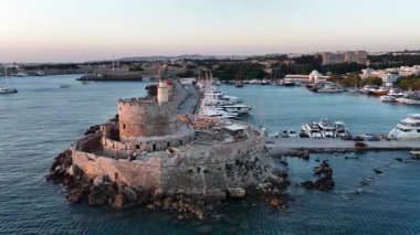 Gün batımında Aziz Nicholas Kalesi 'nin havadan görünüşü. Birçok tekne kaleye giden rıhtım boyunca yanaşan limanı dolduruyor. Rodos şehri arka planda görünür..