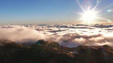 Madeira 'daki Pico do Arieiro' nun yüksek açılı perspektifi. Güneş bulutların üstünden yükseliyor. Aşağıdaki dağlara ışık saçıyor..