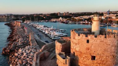 Burası Rodos Yunanistan 'daki Mandraki Limanı' nı gösteriyor. Aziz Niklas Kalesi ve kenetlenmiş pek çok yat görülebilir durumda. Eski taş duvarlar gün batımında aydınlanır..
