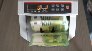 Bir kişi 100 Euro 'luk banknotları saymak için para sayma makinesi kullanıyor. Makine sayarken nota sayısını gösterir.