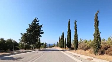 Yunanistan 'da dar bir yolda sakin bir yolculuk. Ağaçlarla çevrili ve güzel mavi bir gökyüzü. Uzakta deniz var. Güneşli bir günde yakalandı.