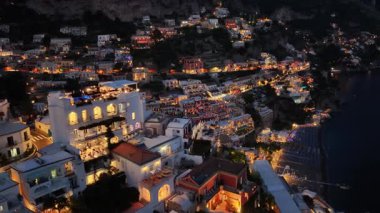 Positano kasabası geceleri sıcak bir şekilde parlar. Yamaçta evler ve binalar aydınlatılır. Karanlık denizde dinlenen teknelerle Amalfi kıyısında ışıklar parıldıyor..