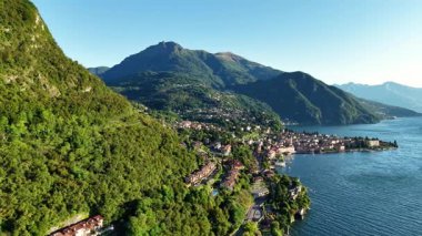 Güneşli göl köyü insansız hava aracı yaklaşırken dolambaçlı dağ yolu teras evler zümrüt ormanı sakin su