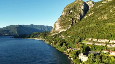 Derin mavi göle bakan dramatik uçurum kıyısı, dik kaya yüzeyi, dolambaçlı kıyı yolu ve dağınık