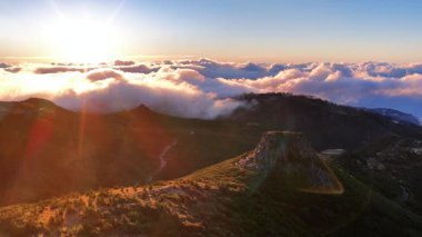 Madeira Portekiz 'deki dağ zirvelerinin havadan görünüşü. Güneş bulutlardan oluşan bir denizin üzerinden yükselir ve manzaranın üzerine altın bir ışık saçar..