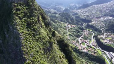 Bir vadinin havadan bir perspektifini görüyoruz. Madeira 'nın dolambaçlı yolları boyunca uzanan evleri ve köyleri çevreleyen yeşil dağlar. Güneşli bir gün..