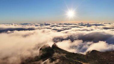 Bulutlardan oluşan bir denizi delip geçen dağ zirveleri manzarası. Güneş gökyüzünde ışıl ışıl parlıyor. Madeira Portekiz 'de sabahın erken saatlerinde atmosfer.