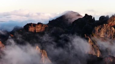 Sis zerreleri Madeira 'nın kayalık dağ manzarasında hareket eder. Sabah ışığı tepelere turuncu bir ışık veriyor. Sahne huzurlu ve huzurlu..