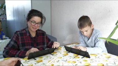 Bir anne ve oğul, tabletlerini kullanarak limon desenli bir masa örtüsüyle masada oturuyorlar. Yoğunlaşıyorlar gibi görünüyor. Belki de evlerinde ödev yapıyorlardır..