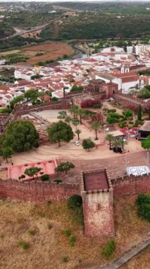 This shows a view from above Silves Castle. The aged stone walls and structures stand out against the backdrop of the city and landscape in Algarve Portugal.
