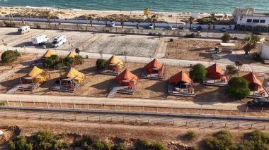 İnsansız hava aracı Algarve 'deki kamp alanının görüntülerini kaydediyor. Aydınlık bir günde arka planda araçları ve binaları olan turistler ve kampçılar için deniz kenarında çok sayıda çadır kuruldu..