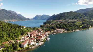 Bu İtalya 'daki Como Gölü' ndeki bir kasabanın havadan görünüşünü gösteriyor. Arka planda dağlar var. Tekneler gün boyunca açık bir gökyüzünün altında gölde seyahat ederler..