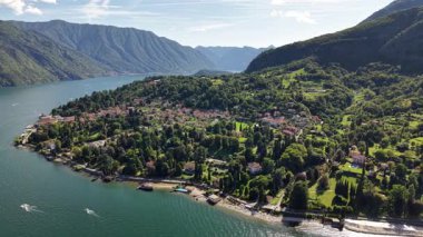 Hava görüntüsü İtalya 'daki Como Gölü' nü gösteriyor. Arka planda dağlar yükselir. Çiçekli ağaçlar ve villalar manzarayı işaretliyor. Tekneler güneşli bir günde denizde seyahat eder..