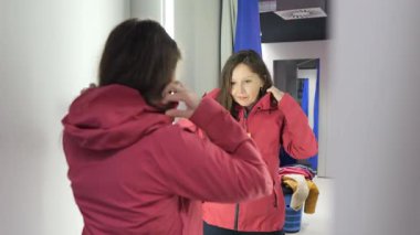 Bir kadın soyunma odasında kırmızı ceketi deniyor. Ceketin düğmelerini ilikliyor ve aynaya bakarken yakasını düzeltiyor. Nöbeti kontrol ediyor gibi görünüyor..