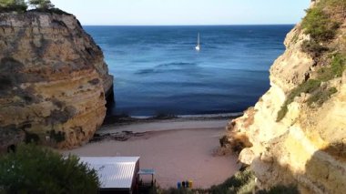 Havadan bakıldığında, Portekiz 'deki Ponta da Piedade yakınlarında engebeli kayalık kumlu plajlar ve turkuaz su sergilenmektedir. Güneşli bir öğleden sonra tek bir yelkenli ufku süslüyor..