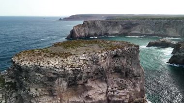 Dalgalar kıyı kayalıklarına çarpar. Kaya oluşumları koyları oluşturur. Algarve bölgesi manzarası. Gündüz çekimleri.