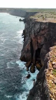 Sahil manzarası ve Sagres Portekiz yakınlarındaki uçurumlar. Dalgalar kıyıya vuruyor ve gün ışığında kayalık kayalıklar boyunca çarpışıyor. Kıyı şeridi mesafeye kadar uzanıyor..