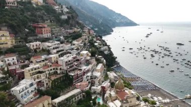 Positano İtalya kıyı kasabasının hava manzarası. Evler tepenin yamacında. Tekneler suyun içinde. Kumsal sandalyelerle dolu..