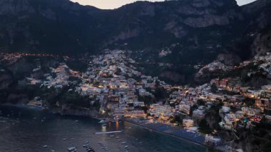 Alacakaranlıkta İtalya 'nın kıyı kenti Positano' nun hava manzarası. Suda yüzen tekneler gibi binalar aydınlanıyor..