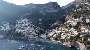 Yüksek açı, Positano İtalya 'yı gösteriyor. Tekneler denizde yüzer. Binalar dağa kadar uzanıyor. Gökyüzü gün boyunca açık.