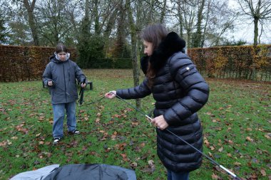 İki kişi arka bahçede çadır kuruyor. Bulutlu bir sonbahar günüdür ve düşen yapraklar çimenlere saçılmıştır..