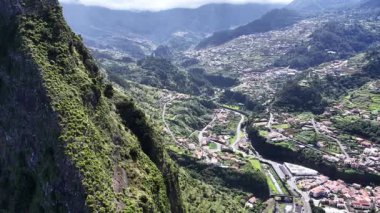 Üstgeçit Madeira engin yeşil dağları, derin vadileri ve açık gökyüzünün altında dolambaçlı yolları olan canlı bir kasabayı gösteriyor..