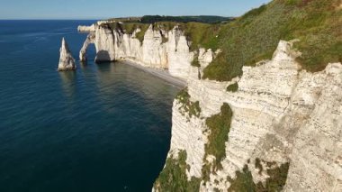 Etretat Fransa 'nın ikonik beyaz tebeşir uçurumlarını, doğal kemerleri ve berrak gökyüzünün altında sakin bir okyanusu gösteren hava perspektifi.